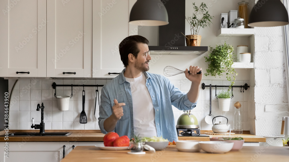 Happy young energetic man singing favorite song in kitchen utensils as microphone, preparing breakfast at weekend. Handsome millennial guy having fun, involved in domestic playtime activity. Happy young energetic man singing favorite song in kitchen utensils as microphone, preparing breakfast at weekend. Handsome millennial guy having fun, involved in domestic playtime activity.