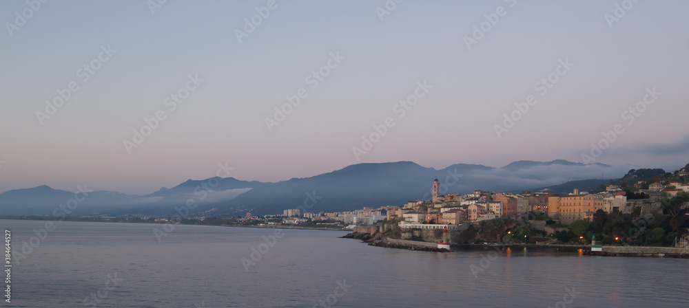 Early morning sunrise over the Mediterranean Sea, Corsica, and the city of Bastia with purple clouds over the mountain.