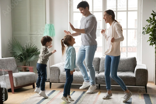 Happy young Caucasian family with two small preschooler kids dancing together in living room in new home. Excited parents with little children renters have fun jump enjoy leisure active weekend.