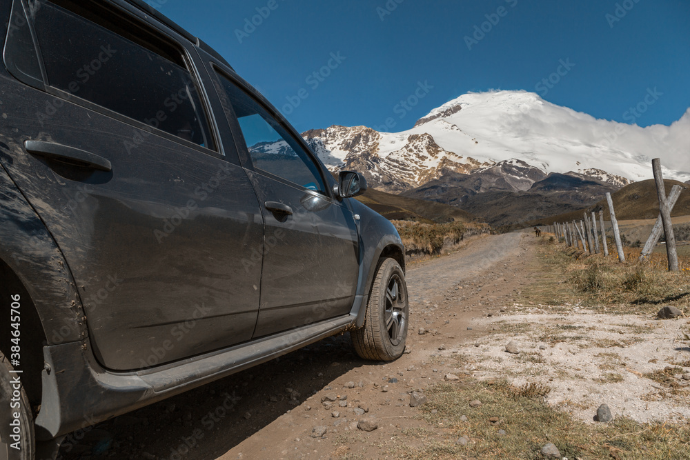 a black car, in the field, a dirt road, in the background is a snow-covered mountain, clear sky, sunny day