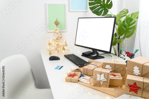 Christmas Shopping online with a credit card. Christmas gifts and a computer monitor on a table in a home office. Winter holidays sales. Long-distance gifting.