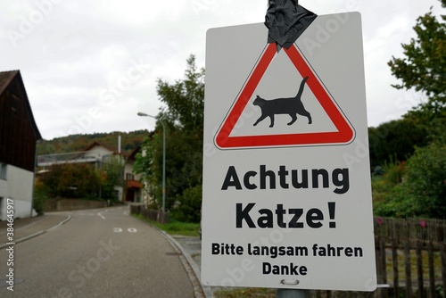 A traffic sign saying in German language: attention, beware of a cat, please drive slowly, thank you. The sign is located in town Weinfelden in Switzerland, in residential district with speed limit. photo