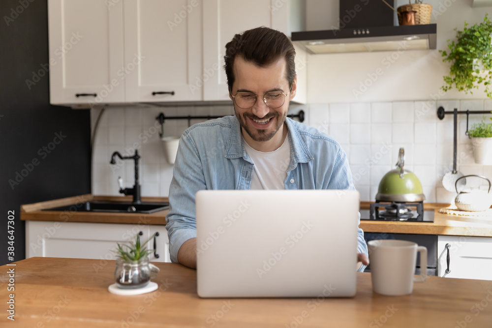 Happy young handsome man in eyewear sitting at kitchen table, involved in online  dating communication con computer. Smiling millennial guy using electronic  gadget laptop, watching funny video. Stock Photo | Adobe Stock