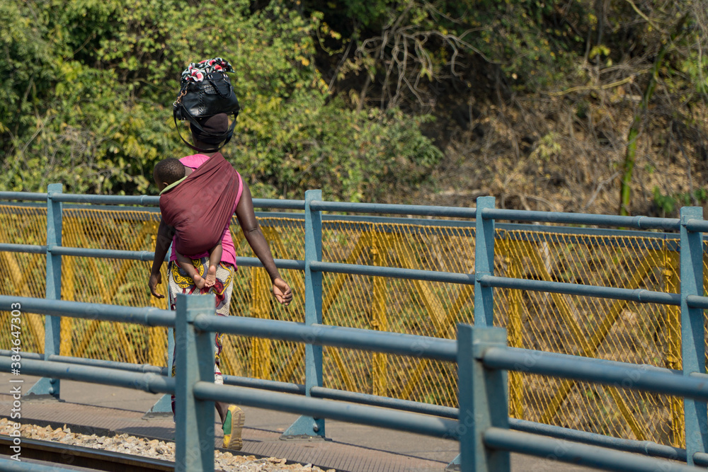 Woman with baby crossing thee bridge between ZAMBIA and ZIMBABWE - obrazy, fototapety, plakaty 