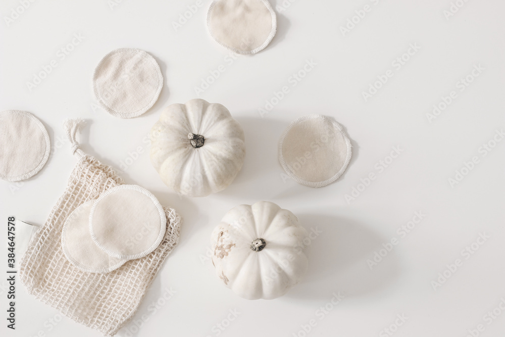 Bio organic cotton reusable round pads for make up removal with pumpkins and knitted bag on white table background. Zero waste concept. Sustainable bathroom and lifestyle. Flat lay, top view. Bio organic cotton reusable round pads for make up removal with pumpkins and knitted bag on white table background. Zero waste concept. Sustainable bathroom and lifestyle. Flat lay, top view.