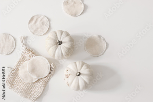 Bio organic cotton reusable round pads for make up removal with pumpkins and knitted bag on white table background. Zero waste concept. Sustainable bathroom and lifestyle. Flat lay  top view.