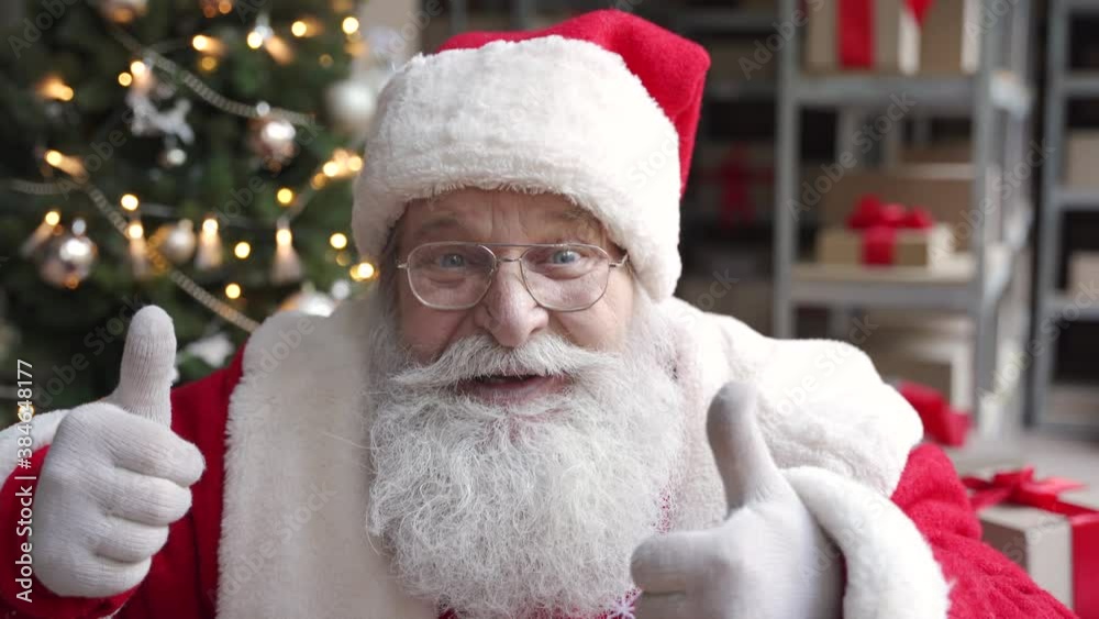 Funny old bearded Santa Claus, Saint Nicholas talking to camera greeting on Merry Christmas Happy New Year, standing in warehouse workshop, video calling by webcam online virtual chat concept.