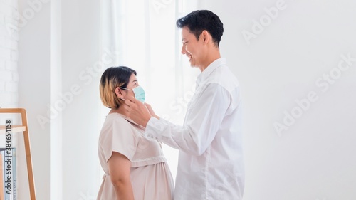 Pregnant Asian women wife wear a protective mask by husband to prevent germs.During the quarantine at home for preventing coronavirus and covid-19 infection.