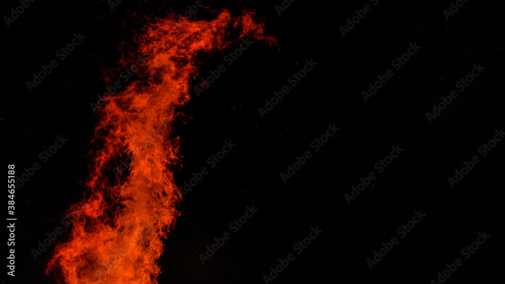 CLOSE UP: A large blaze bursts high into the dark night sky near a campfire.