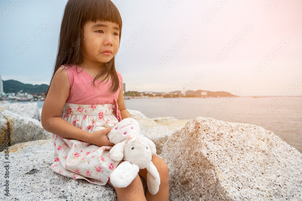 Little girl crying and hug the rabbit doll by the sea in a sad mood and missed her family Little girl crying and hug the rabbit doll by the sea in a sad mood and missed her family