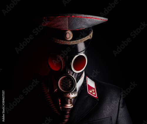 Portrait photo of a post apocalyptic military officer in uniform suit and peaked cap standing in soviet gas mask on black background. photo