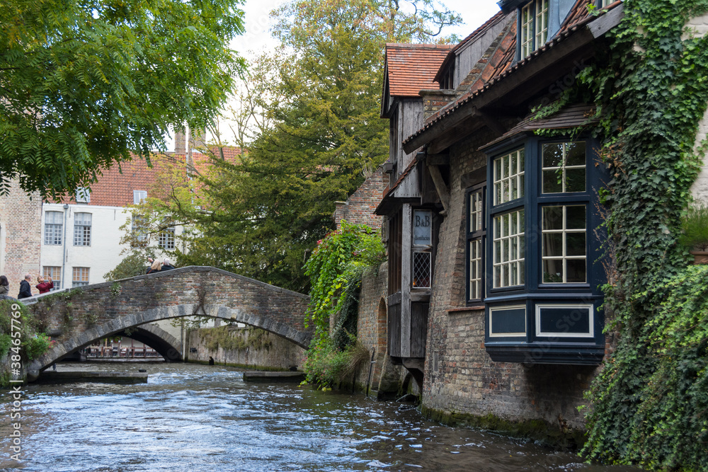 Naklejka premium Belgium, Flanders, Bruges - Brugge. Typical water canal of the city seen from a tourist boat. Cloudy day.