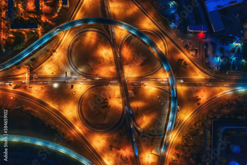 Large roundabout or road transport junction at night with car traffic, aerial top view.