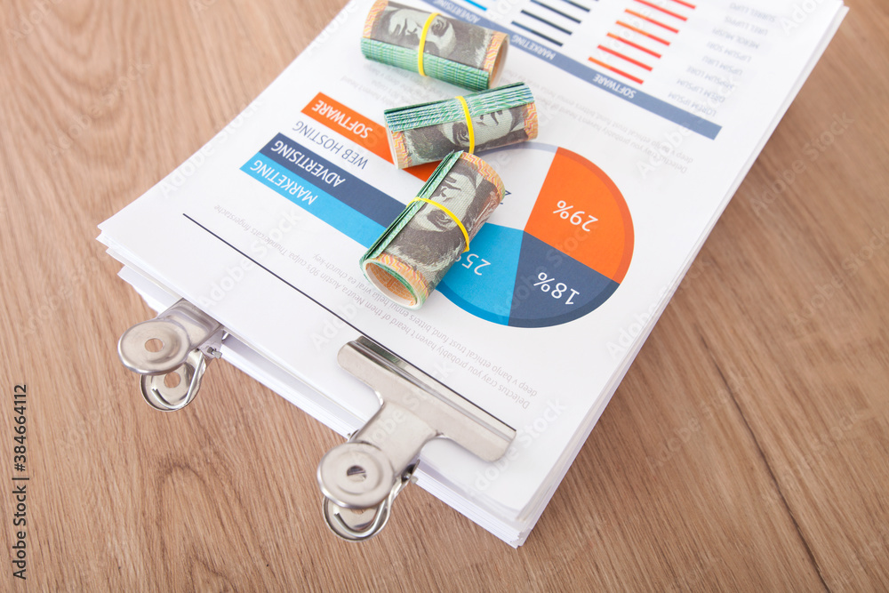 A stack of paper business documents and several rolls of Australian dollar banknotes on paper A stack of paper business documents and several rolls of Australian dollar banknotes on paper