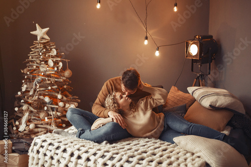 Couple near christmas tree. Lady in a brown sweater. Family sitting on a bed.