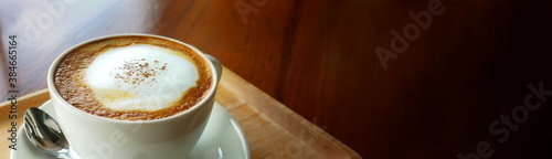 Closeup hot cappuccino coffee cup on dark wooden table with copy space as banner background
