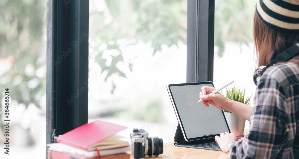 Cropped image of young woman holding digital pen and writing or drawing on tablet scren while sitting at the table in co-workspace. Cropped image of young woman holding digital pen and writing or drawing on tablet scren while sitting at the table in co-workspace.