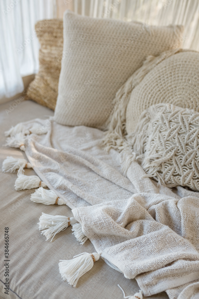 White knit blanket lying on the corner sofa in the living room, macrame pillows around