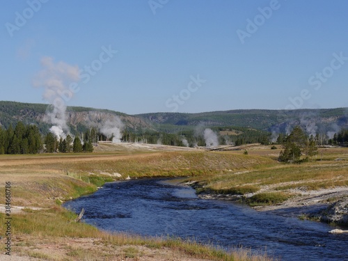Wide shot of the Firehole River with hot water overflow and steam rising from multiple geysers at the Yellowstone National Park in Wyoming.