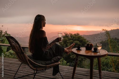 Young woman enjoying glass o white wine on the roof by the mountain terrace at sunset