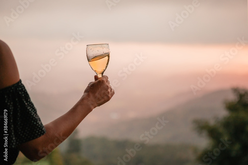 Woman s hand holding glass of white wine across beautiful mountains landscape and sunset