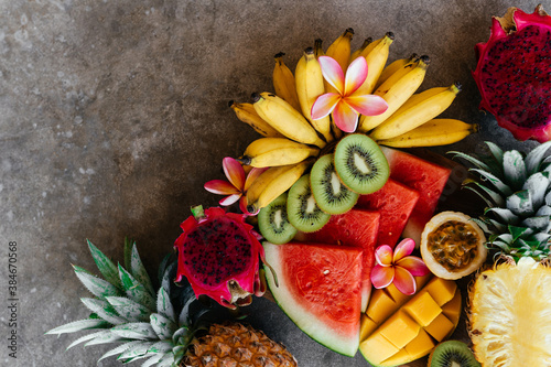 Tropical fruits assortment on a wooden plate. Stone background. Top view. Copy space.