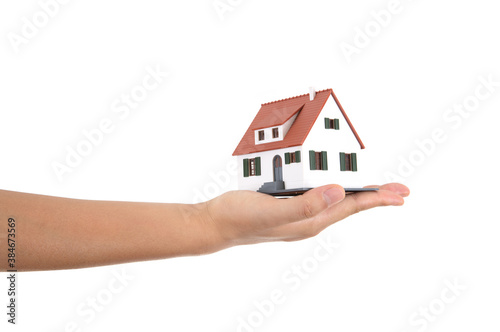 A hand holding a small house model in front of a white background