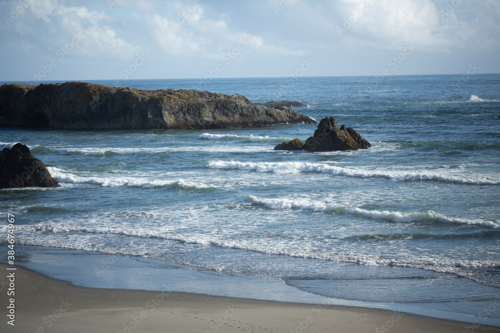 Rolling waves crashing in past ridges of rock on an Oregon beach against a white cloudy sky