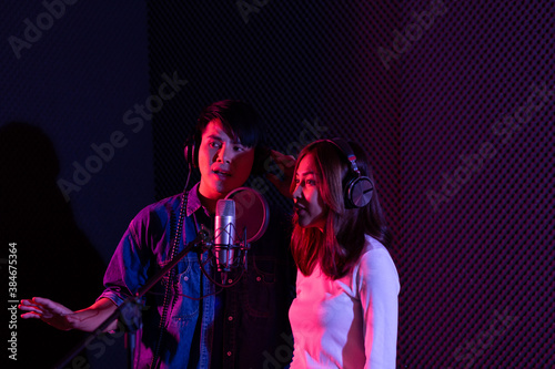 Portrait of asian young woman and man, artist singing into a microphone while recording a song in a studio