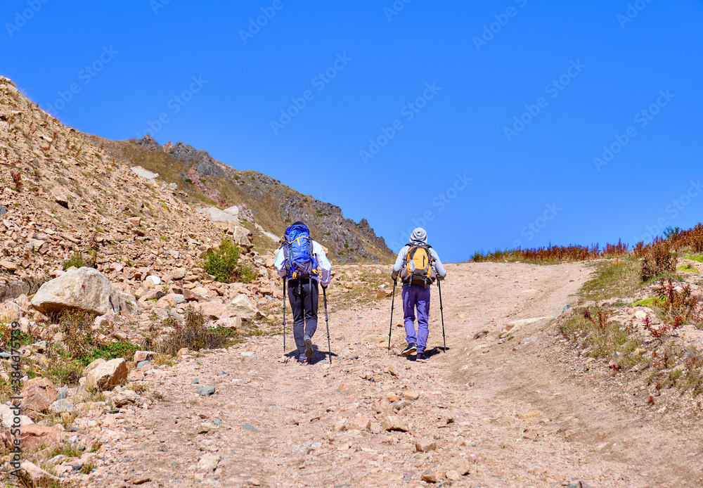 Group of tourists has a trekking on a dirt road in the highlands against a blue sky; active lifestyle concept