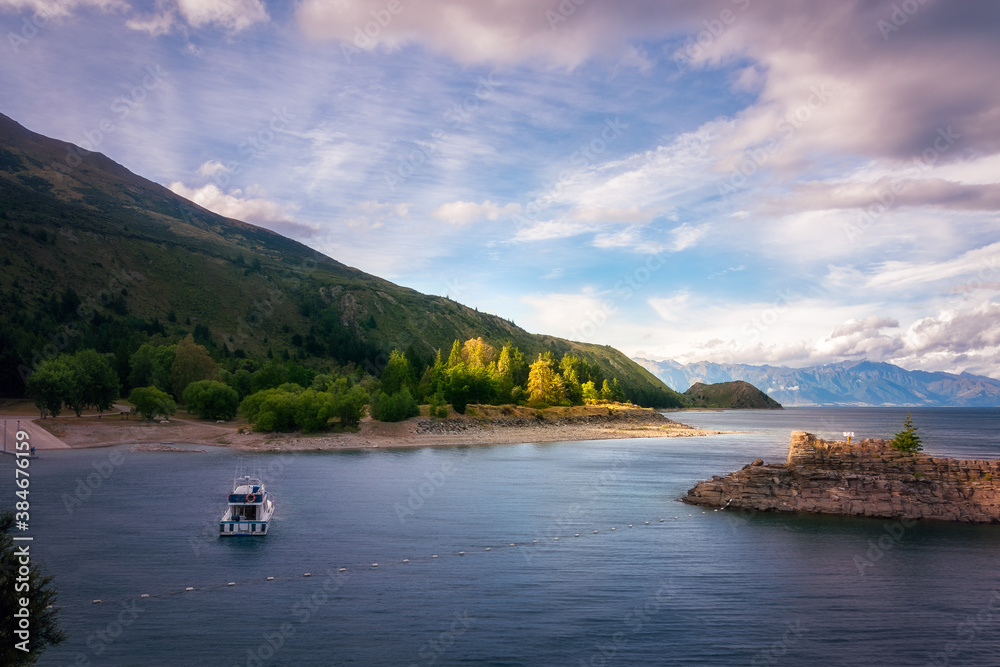 Sunset panorama at the southern end of Lake Hawea with a beautiful patch of backlit trees in the background and a small boat in shade in the foreground - Otago Region, New Zealand, Southern Alps.