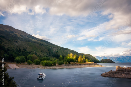 Wonderful sun rays behind the mountain and backlit trees at the southern end of Lake Hawea with a small boat in the foreground in Mount Aspiring National Park, Otago Region, New Zealand, Southern Alp