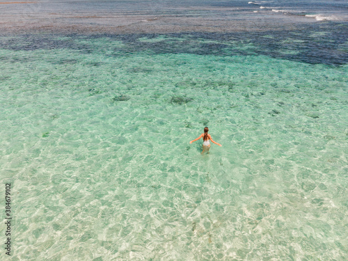 Young woman in a bikini walks to the blue sea, view fom drone, crystal clean water