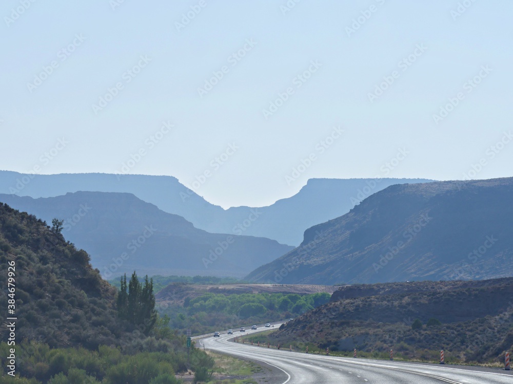 Virgin, Utah--July 2018: Winding road with the faint silhouettes of distant mountains Zion National Park in the late afternoon sun.