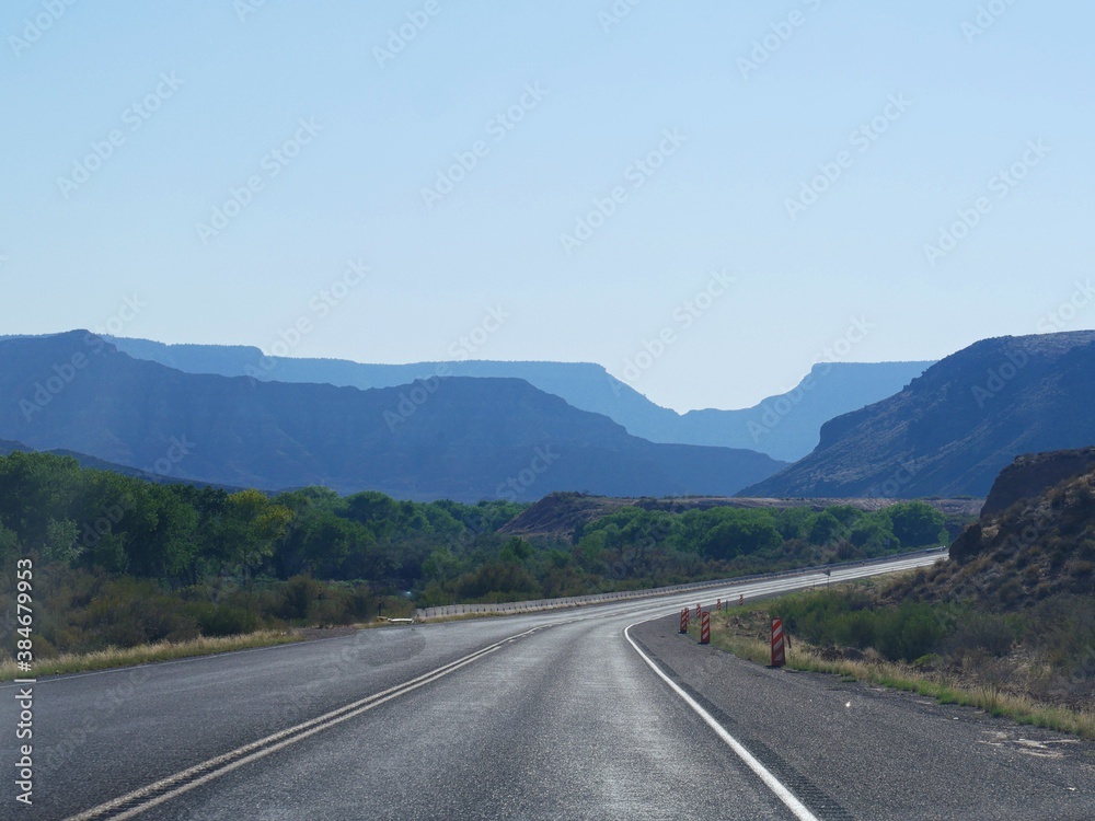 Paved winding road to Zion National Park, with silhouettes of the mountains in varying hues of blue.