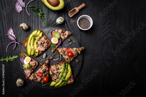 Bruschetta collection with tuna, quail egg, cherry tomatoes, avocado, microgreen and capers on a dark background, Tasty tuna sandwiches. Delicious breakfast or snack. Top view
