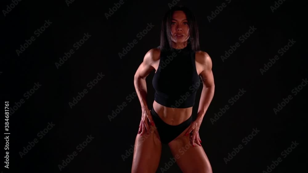Breathtaking front view of a beautiful young brunette in a bikini standing on a black isolated background Breathtaking front view of a beautiful young brunette in a bikini standing on a black isolated background