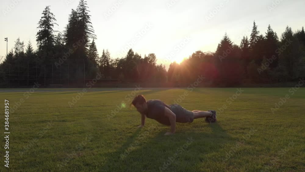 Caucasian man doing pushups in a field at sunset. 4K 24FPS.