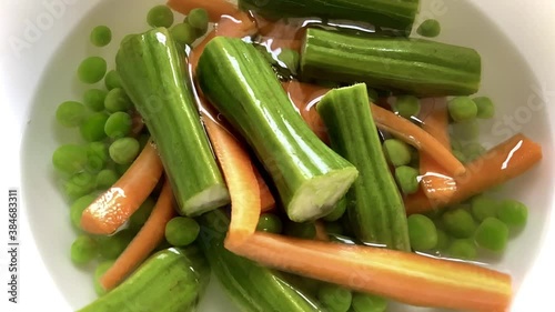 Dropping carrots and drumstick pieces into a dish filled with water and vegetables