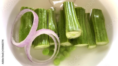 Falling of onion rings tomato slices organic peas and carrots into a dish of drumstick soaked in water 