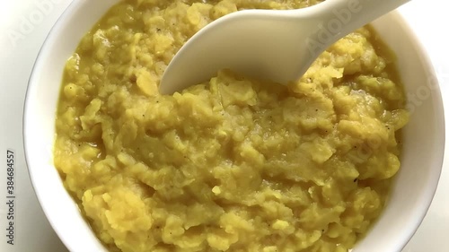 Hot Yellow lentil dal gravy made with split pigeon peas in a white bowl scooped with a white spoon and shown in close up on a white background