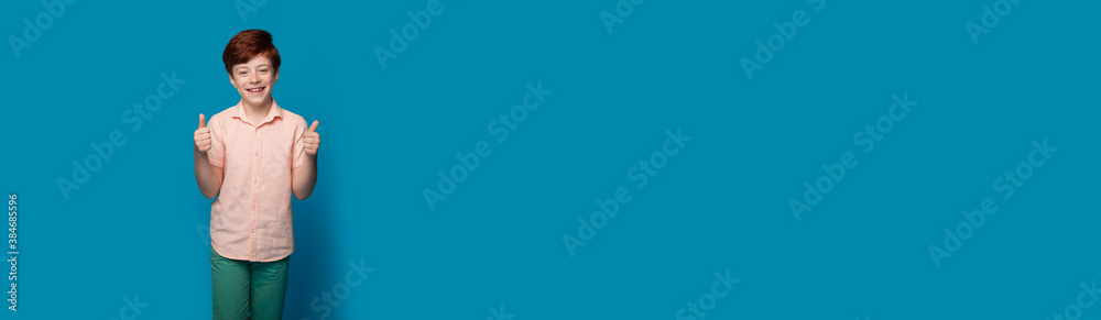 Caucasian boy with red hair is gesturing the like sign on a blue studio wall with free space advertising something Caucasian boy with red hair is gesturing the like sign on a blue studio wall with free space advertising something