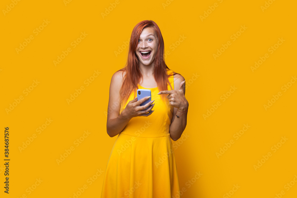 Monochrome photo of a caucasian woman with a dress and red hair pointing to her phone on a yellow studio wall Monochrome photo of a caucasian woman with a dress and red hair pointing to her phone on a yellow studio wall