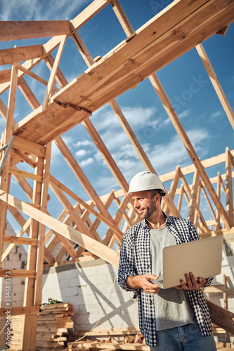 Experienced worker with a laptop posing near building in progress