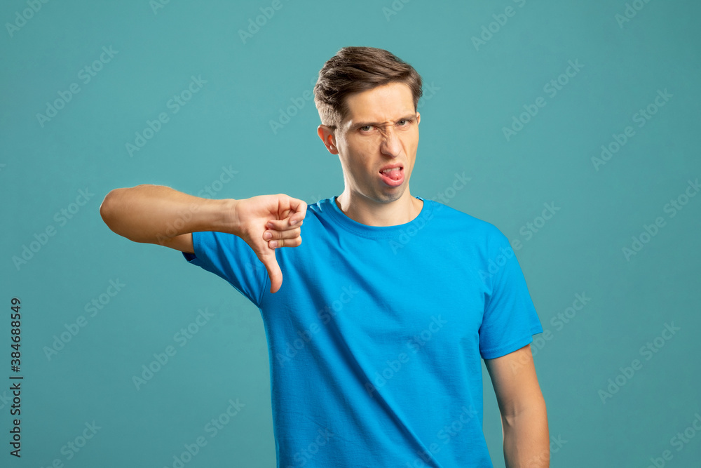 Blaming male portrait. Dislike gesture. Condemnation shame. Bad job. Disgusted expressive man showing thumb down looking at camera isolated on blue.