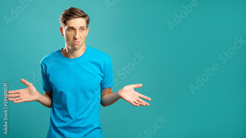 Doubtful male portrait. Careless gesture. Disbelief emotion. Helpless look. Astonished thoughtful young man shrugging looking at camera isolated on blue copy space.