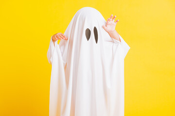 Funny Halloween Kid Concept, Closeup a little cute child with white dressed costume halloween ghost scary, studio shot isolated on yellow background