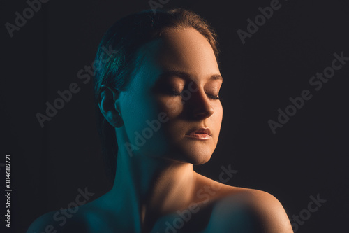Neon light portrait. Beauty correction. Peaceful woman with bare shoulders closed eyes in blue glow isolated on dark copy space background. Aesthetic cosmetology. Skin rejuvenation.