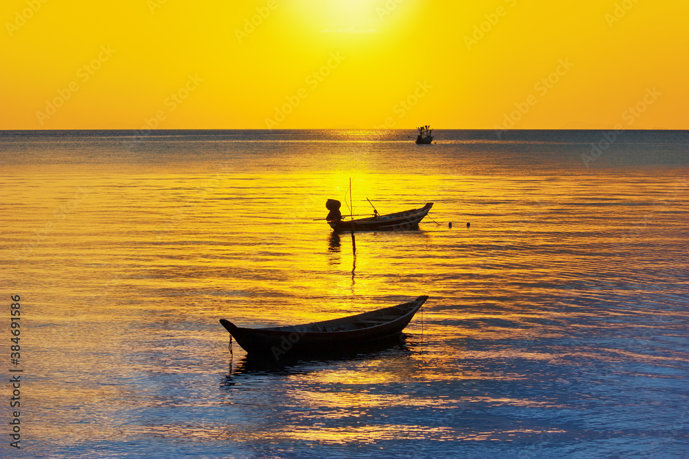 Fototapeta premium Beautiful sunset landscape, yellow sky, golden sun glow reflection on water, fisherman boats silhouette on blue sea background, ships on ocean beach, sunrise seascape, travel in Thailand, Samui island