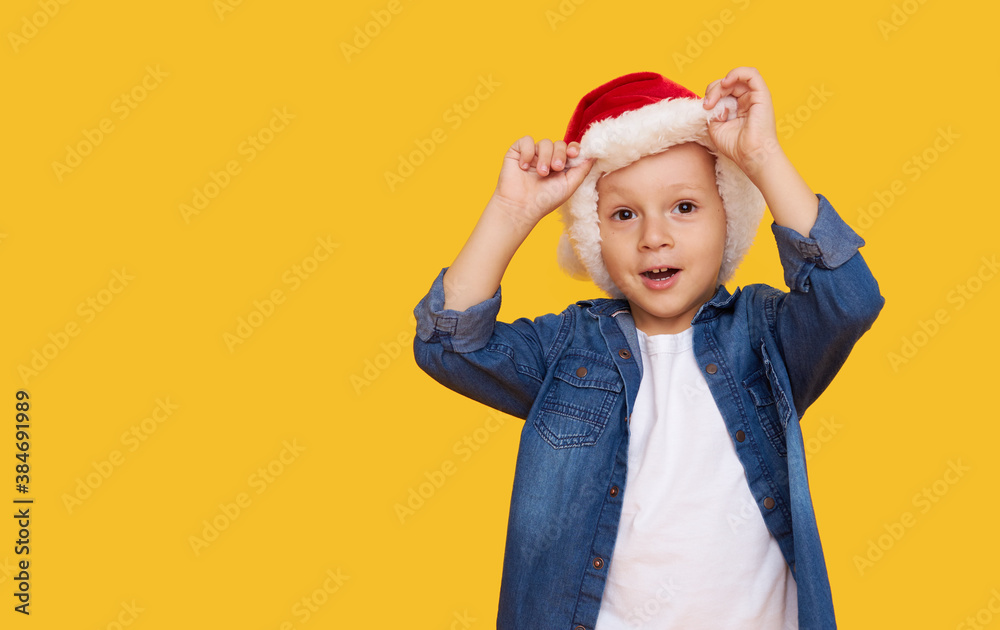 Portrait of a satisfied little child boy dressed in christmas Santa hat. laughing isolated over colored yellow background. Wow face. Season of discounts Portrait of a satisfied little child boy dressed in christmas Santa hat. laughing isolated over colored yellow background. Wow face. Season of discounts